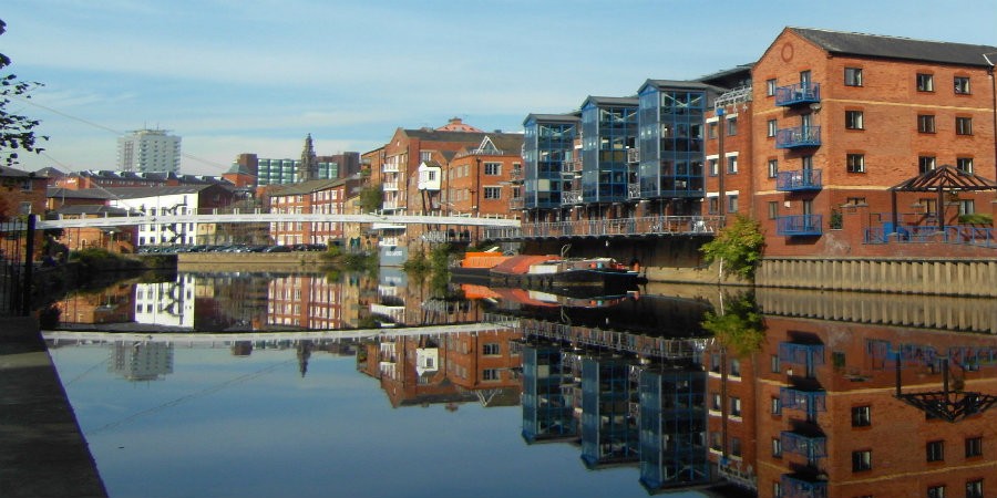 View down River Aire towards Leeds City Centre with moored boats, white bridge and city buildings in background