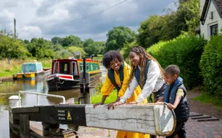 Two women and a boy laugh as they push open a lock beam to let a green and red hire boat in.