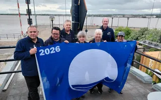 Group of people wearing dark blue jackets holiding up a blue flag