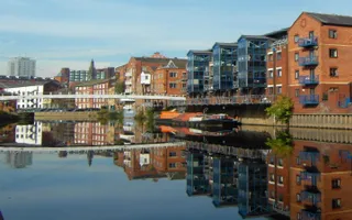 View down River Aire towards Leeds City Centre with moored boats, white bridge and city buildings in background