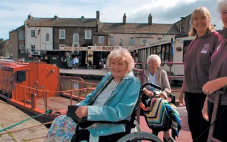 Two women in wheelchairs move from a boat onto the towpath