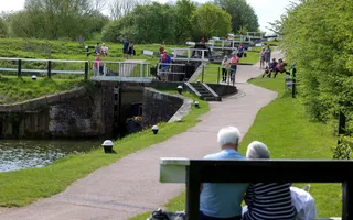 A couple sit on a bench looking out towards a series of lock gates, which are dotted with visitors
