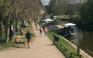 People walk along the towpath in the sun, passing moored boats