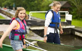 Two girls in life jackets carrying a canoe past a lock gate