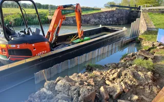Orange digger on a work boat dredging a canal