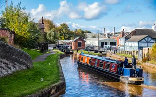 Cloudy but sunny day, boat travelling along canal, green towpaths indicating bridge