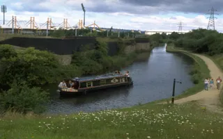 Boat on navigation in front of sports arena, with family walking on towpath