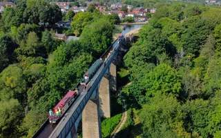 An aerial view of narrowboats crossing the Pontcysyllte Aqueduct, a tall stone structure surrounded by lush greenery.