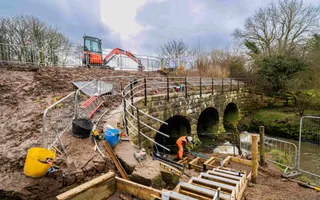 wide shot of a works site at a canal and bridge with lots of mud surrounding the site.