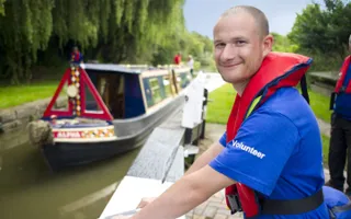 Volunteer lock keeper smiles as he opens the lock gate to let a narrowboat out