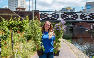 Woman on a sunny canal towpath holding two plants in pots