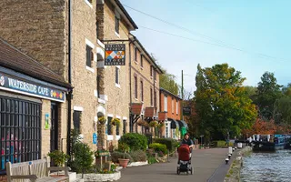 A woman with a pram walks by Stoke Bruerne Canal Museum with the canal on the right