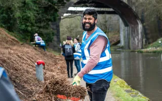 Canal & River Trust volunteer smiling as he shovels grass on the canal towpath