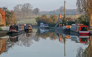 Wide shot of a canal with narrowboats and fields in the background