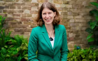 Woman in a green suit posing for photo infront of a brick wall