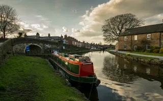 Narrowboat moored along canal lined with housing with a stone bridge behind