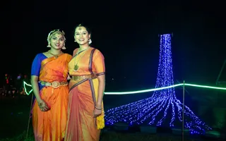 Two women in orange dresses standing infront a stream of fairy lights
