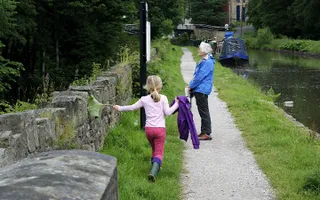 Child skips along the towpath while an adult reads a sign on the Macclesfield Canal at Bollington