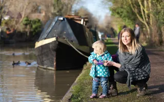 A toddler feeds the ducks on the water as their mother crouches beside her
