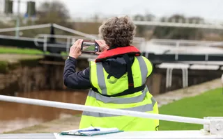 Volunteer, with back towards camera, taking pictures on her phone of the canal water levels