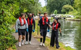 4 young adults walking on towpath, volunteering. All wearing life  jackets, one holding a broom