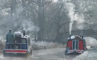 Two boats in winter with smoke blowing out of their chimneys.