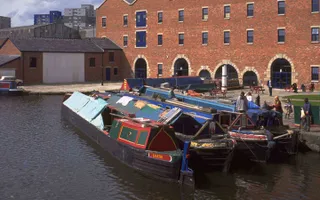 Traditional working narrowboats moored by redbrick warehouse on Ashton Canal