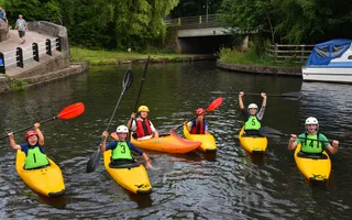Six children in yellow kayaks in a canal