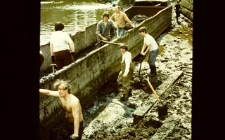 Archived photo of 1970s workers standing in mud next to a boat