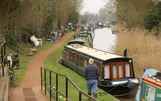 Picture of a row of moored boats with a man and his dog walking along the towpath