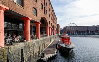 A red boat is moored next to an historic building with red pillars and brickwork