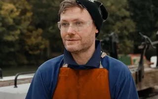 Apprentice wearing red apron standing by canal