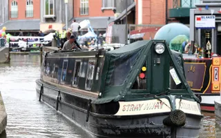 Narrowboat moves passed moored boats and canal-side buildings in busy stretch of the canal.