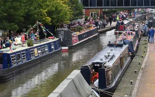 Narrowboats decorated in bunting line the towpath with crowds walking by