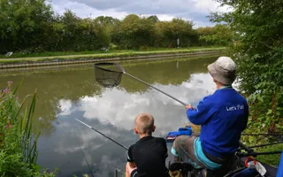 Adult and child fishing next to a canal in the rural countryside