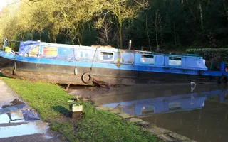 Narrowboat sits sideways in the canal with its nose out of the water and on the bank after flooding
