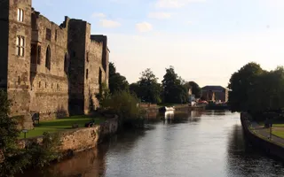 A wide river flows gently passed an stone castle in the setting sun.