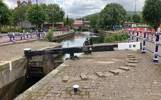 A black and white lock gate surrounded by brick towpath and a canal running underneath
