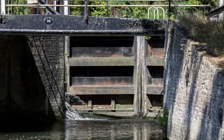 A close up of a large wooden lock gate with water spouting through the side.