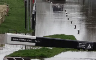 Submerged grass and towpath due to flood water from the overflowing canal surrounds a lock beam.