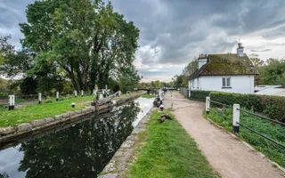 An empty lock with the top gates open, lined by trees and a lock keeper's cottage.
