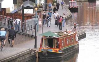 Walkers and cyclists use the towpath in Birmingham, alongside several moored narrowboats.