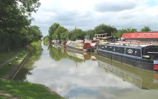 Boats moored on the offside of the canal on the Aylesbury Arm with an angler in the distance on the towpath