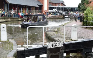 Narrowboat approaches lock as crowds walk by on the towpath