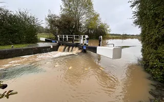Canal water floods surrounding towpath and overflows a lock