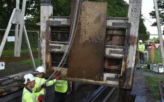 Workers in high vis and hard hats lower a new lock gate into a lock with scaffolding and ropes.