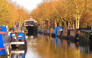 Sun shines on the canal with boats moored on both sides leading to a tunnel