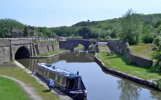 Narrowboat moored on the towpath at a junction in front of a tunnel and bridge under a blue sky