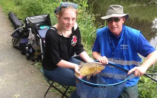 Let's Fish! coach next to a girl holding a fish she's caught in a net