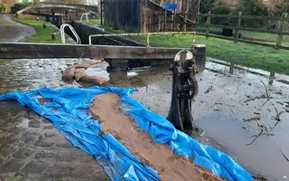 Flooded water tops the bank at Wychnor Lock on the Trent & Mersey with sandbags and tarp on the towpath to prevent damage.